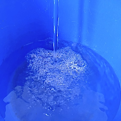 Eimer-mit-Wasser-in-den-heisses-Wasser-gegossen-wird-um-es-fuer-die-Fensterreinigung-vorzubereiten